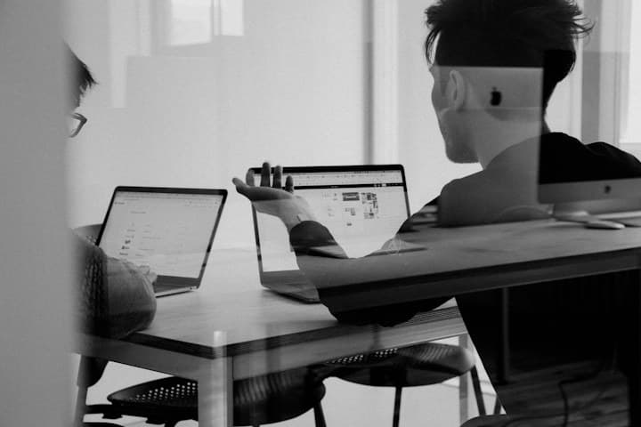 Two colleagues working on connected laptops in an office